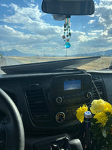 RV rental interior on a road trip. Dashboard with audio and flowers, open road to mountains, and a cloudy sky visible through the windshield.