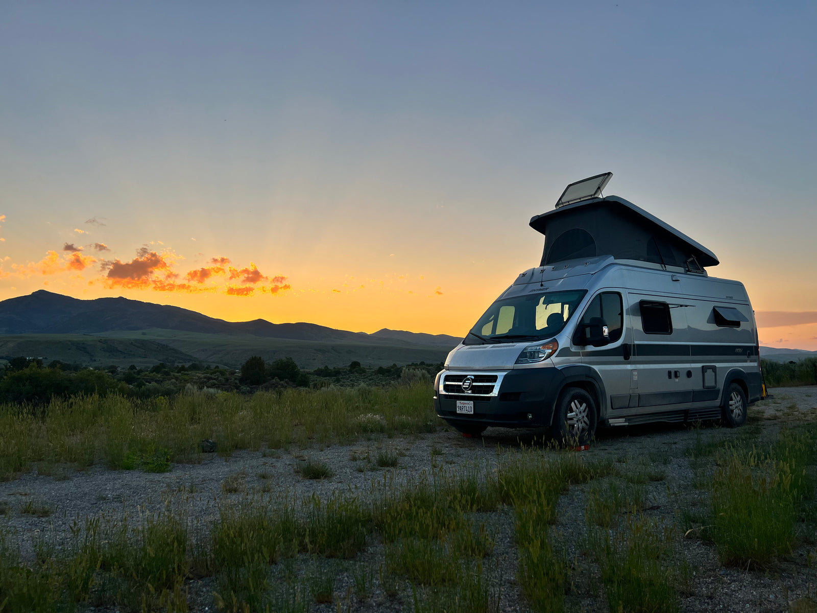 RV rental camper van with pop-top roof on a dirt road at sunset, mountains in background. Perfect for travel & camping.