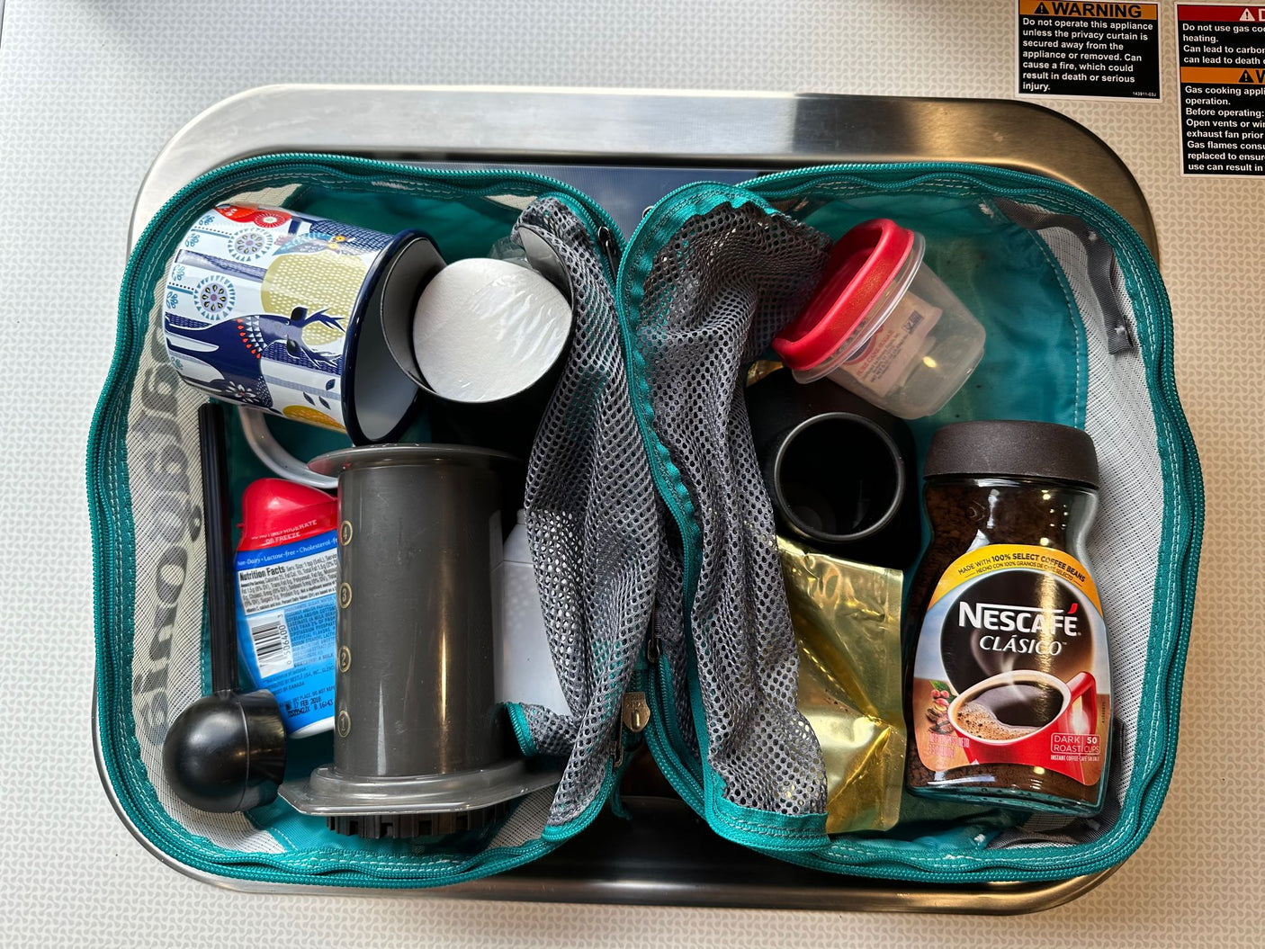 Compact coffee kit for an RV rental, showing AeroPress, Nescafe, mug, and creamer inside a teal bag.