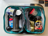 Compact coffee kit for an RV rental, showing AeroPress, Nescafe, mug, and creamer inside a teal bag.