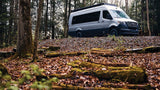 Silver Mercedes Sprinter camper van on a leaf-covered forest hill, ideal for an RV rental outdoor adventure.