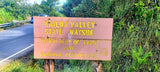 Wailua Valley State Wayside sign next to a road, with a white RV rental or vehicle visible in the background.
