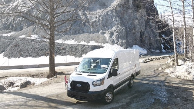 White van, ideal for RV rental, parked on a snowy mountain road with rocky terrain.