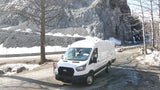 White van, ideal for RV rental, parked on a snowy mountain road with rocky terrain.