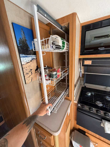 RV rental kitchen: A hand pulls out a multi-tiered pantry rack, optimizing storage for food and supplies.