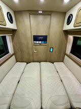 Spacious rv rental interior showing four white quilted beds, a smart TV with streaming, and control panel. Comfortable travel van setup.