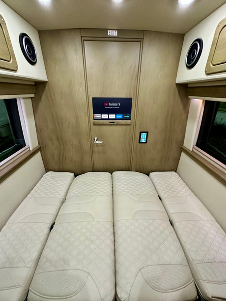 Spacious rv rental interior showing four white quilted beds, a smart TV with streaming, and control panel. Comfortable travel van setup.