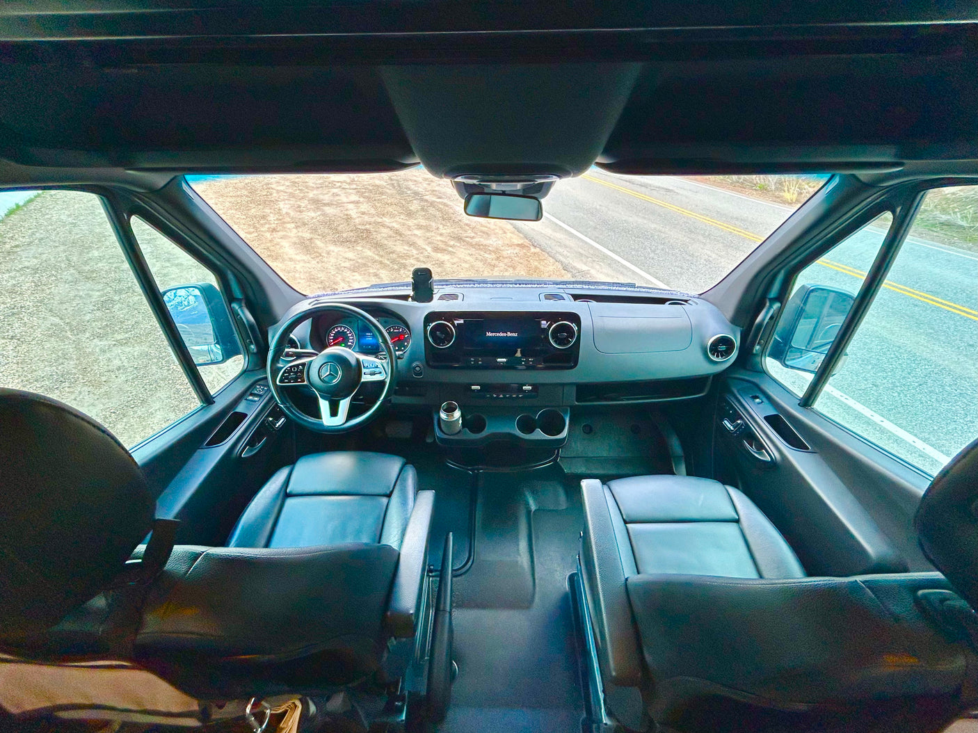 Spacious RV rental cockpit: black seats, Mercedes-Benz dashboard, and clear road ahead for your adventure.