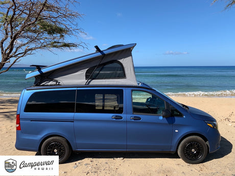 Blue RV rental campervan with pop-top on a sunny beach with ocean views. Ideal for Hawaii outdoor adventures.