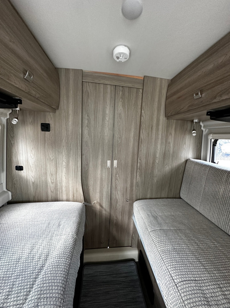 RV rental interior: light wood flooring and cabinetry, plush gray seating, a clear aisle, and safety devices. A modern camper living space. — photo 20