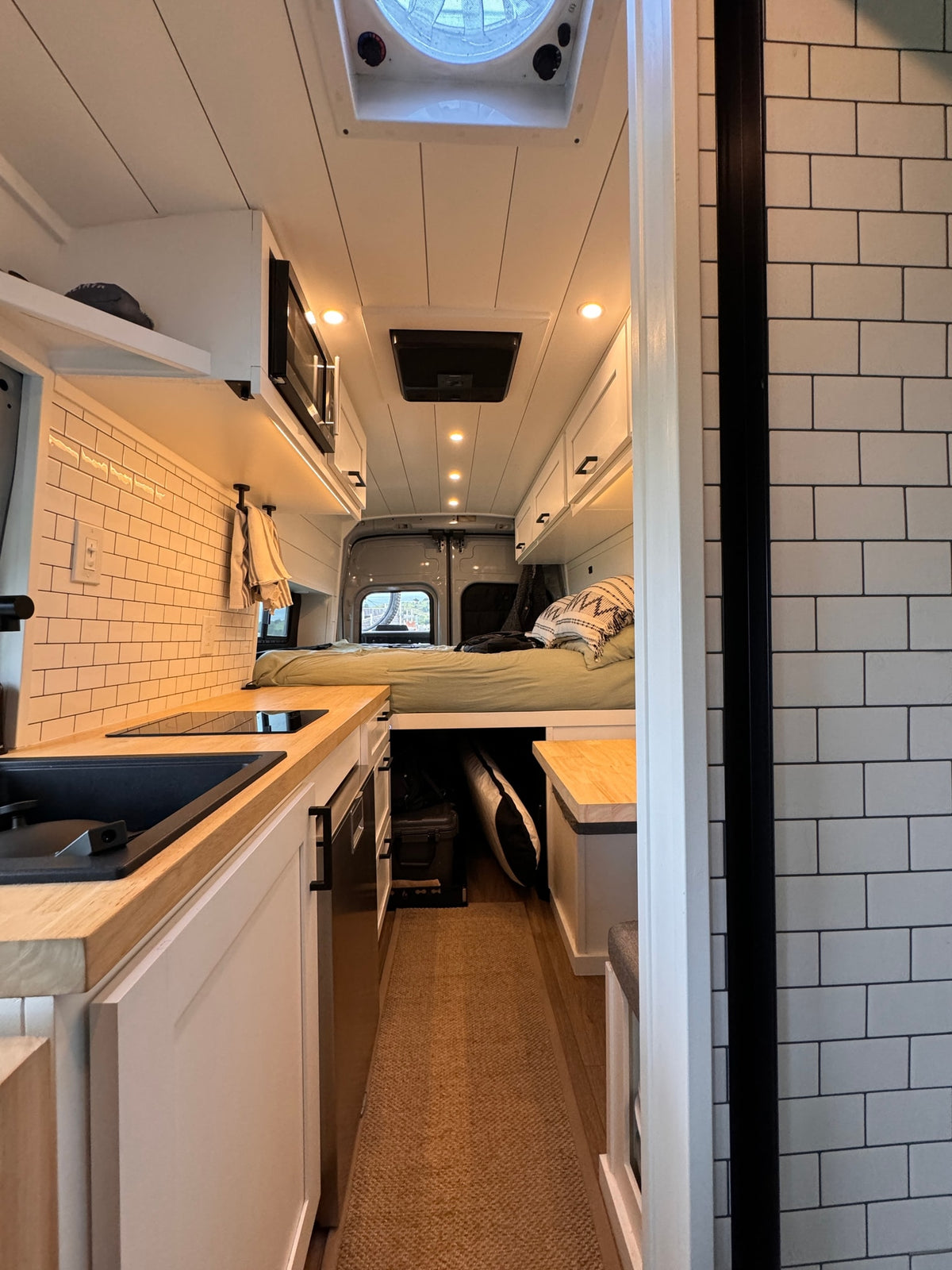 Modern camper van interior with kitchen, bed, and white subway tile backsplash, ideal for rv rental or van life. — photo 6
