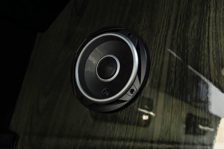 Close-up of a circular speaker with silver trim, installed in a dark wood panel, typical of an RV rental interior.