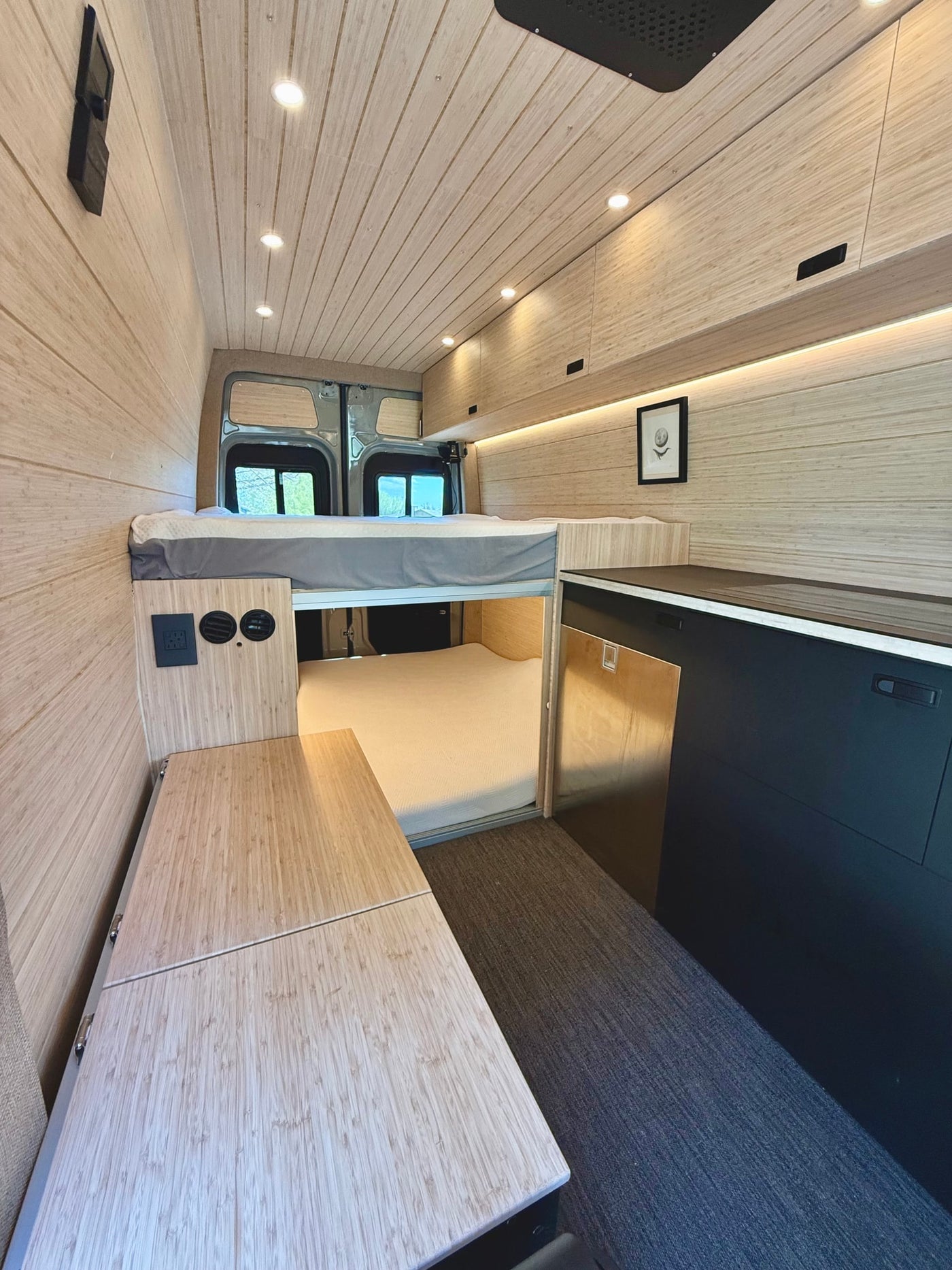 RV rental featuring a sleek camper van interior with natural wood paneling, an elevated bed, and compact kitchen. — photo 10