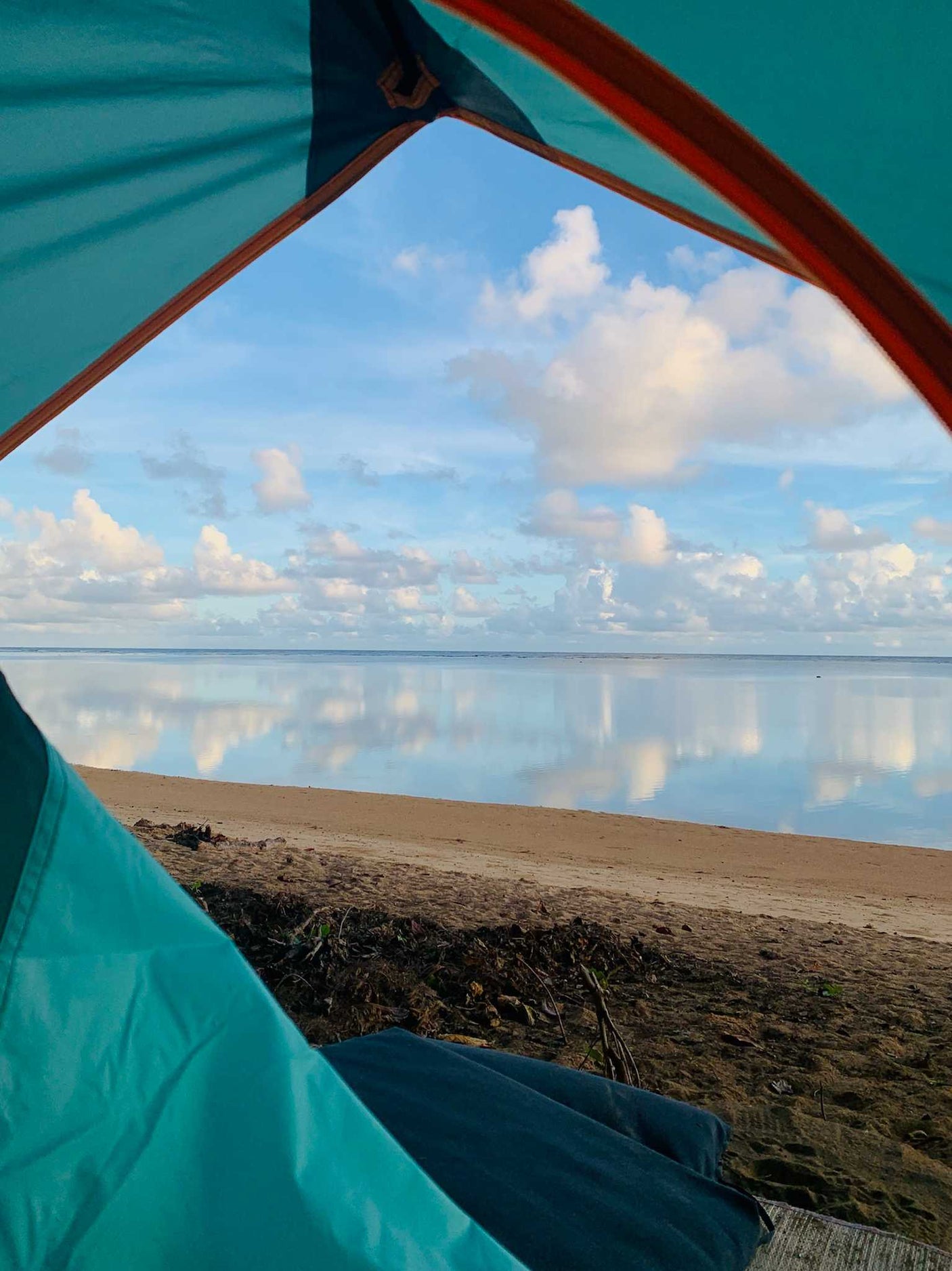 View from inside a tent, showing a serene beach & calm ocean mirroring the cloudy sky. Perfect for an RV rental escape.