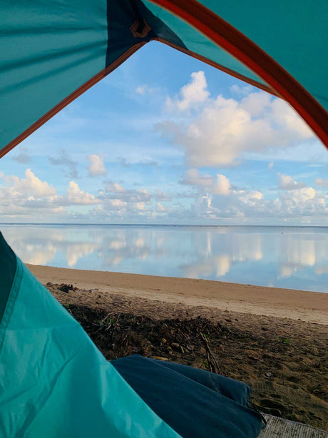 View from inside a tent, showing a serene beach & calm ocean mirroring the cloudy sky. Perfect for an RV rental escape.