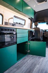 Modern rv rental interior: sleek green cabinets, microwave, fridge, sink, and wood countertop. Spacious camper van kitchen.