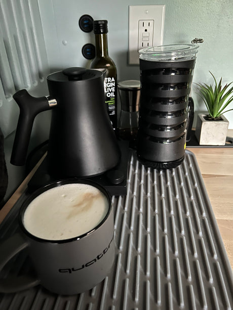 RV rental morning: creamy latte in a "Quattro" mug with a Fellow kettle & frother on a drying mat. Compact coffee setup.