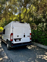 White Ram ProMaster camper van, great for rv rental, parked on asphalt with sunlit trees in the background.