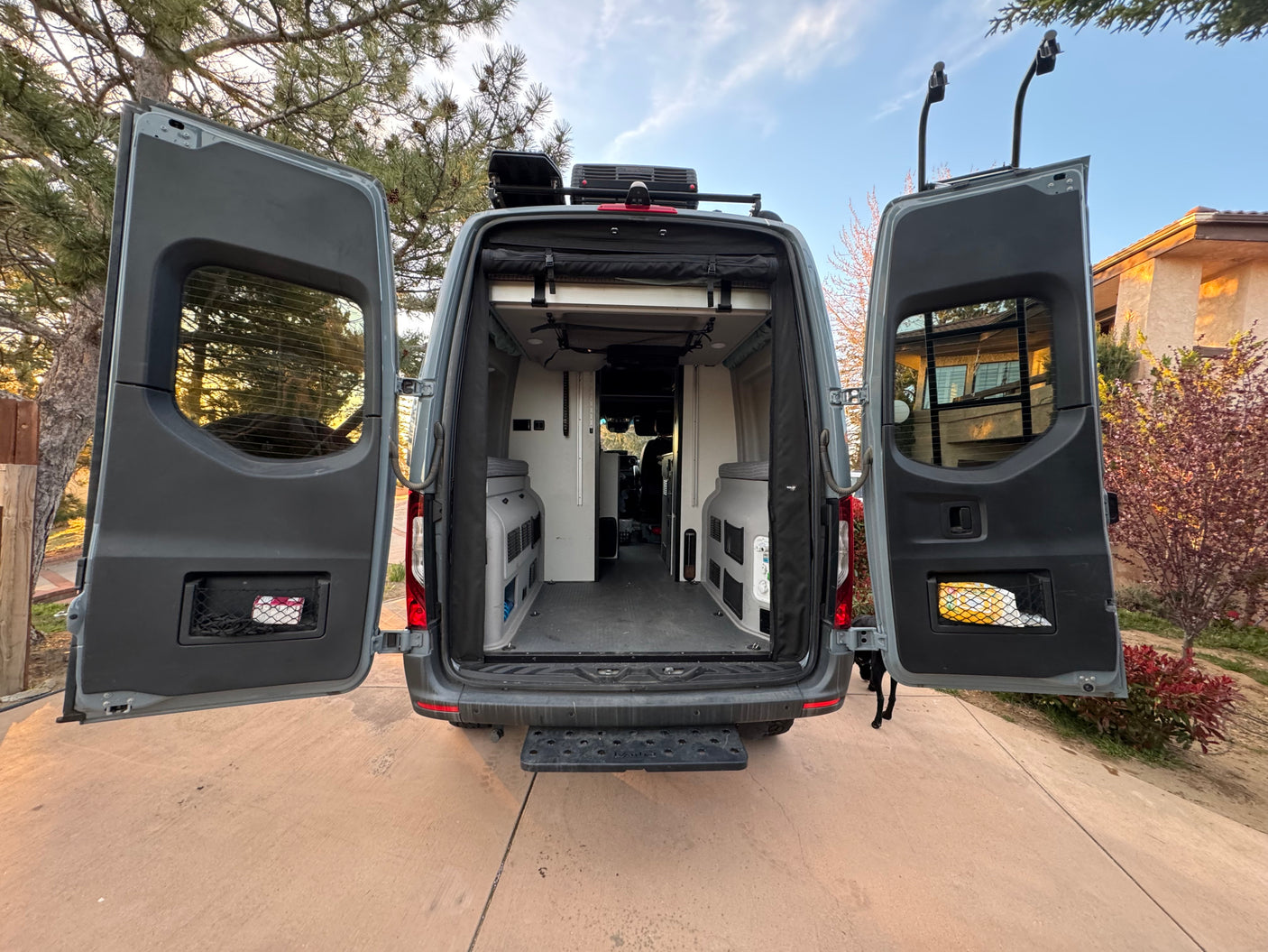 Spacious rear interior of a gray custom camper van with both back doors open, revealing modular storage units. Ideal for rv rental adventures.