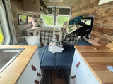 Cozy RV rental campervan interior featuring a comfy bed with nature-themed decor, kitchen, and wood paneling.