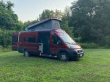 A red Winnebago Solis camper van with an extended pop-top is parked in a grassy field, perfect for an RV rental outdoor adventure.