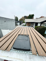Overhead view of an RV rental's custom rooftop deck. Wooden slats surround a black roof vent, enhancing outdoor space.