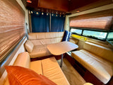 Cozy RV rental interior featuring a dinette with cream leather seating, a table, and windows with blinds and blue curtains.