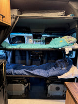 Cozy RV rental interior with two bunk beds, upper and lower, set up for sleeping in a camper van.