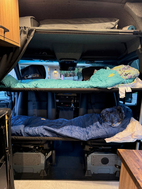 Cozy RV rental interior with two bunk beds, upper and lower, set up for sleeping in a camper van.