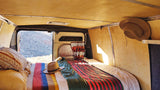 Cozy RV rental van interior with bed & scenic desert views from open back doors.