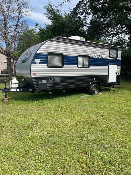 A gray & blue Wolf Pup travel trailer, ready as an RV rental, parked on a green lawn.