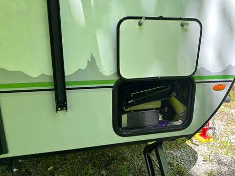 RV rental with open storage hatch displaying outdoor gear & nature-themed decals on its side.