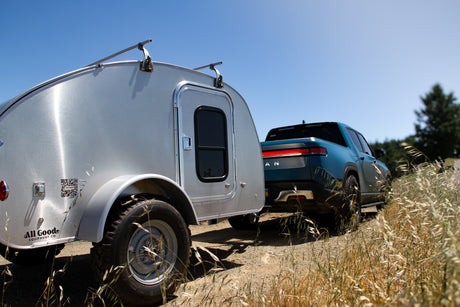 Teardrop RV rental attached to a Rivian electric truck, ready for off-road adventures.