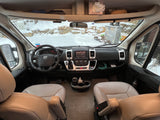 Cozy rv rental interior looking out at a snowy winter landscape. Dashboard, steering wheel, and front seats visible.