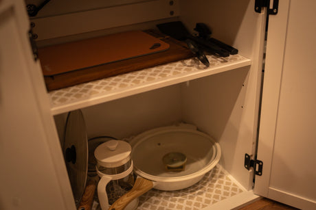 RV rental kitchen cabinet, neatly organized with cutting boards, utensils, a French press, and a cooking pot.