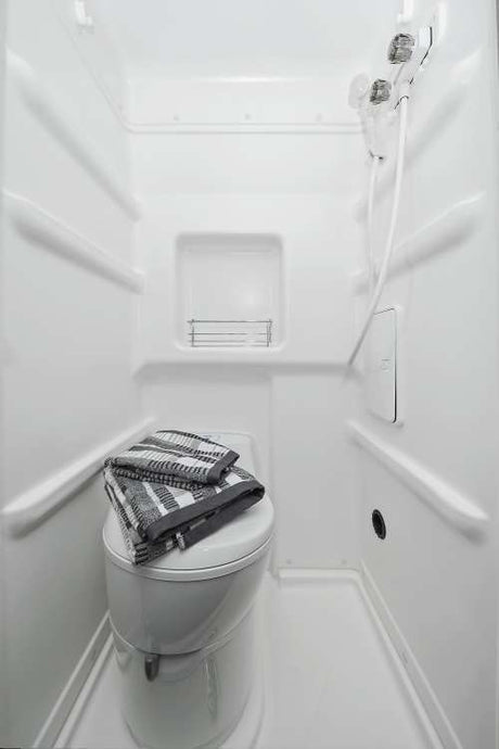 All-white compact wet bath in an RV rental, showing a toilet with towels and a shower.