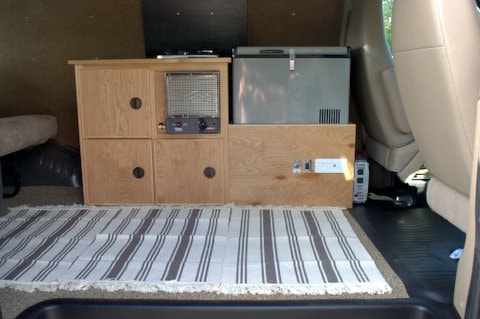 An RV rental's well-organized interior: custom wood cabinets, a portable fridge, heater, and electrical outlets. — photo 4