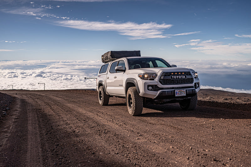White Toyota Tacoma with rooftop tent on a high mountain dirt road, above the clouds. Ultimate adventure, like an RV rental for rugged travel. — photo 10