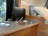 Inside an RV rental: a compact kitchenette featuring a Dometic sink, faucet, countertop, and an adjacent bed area.