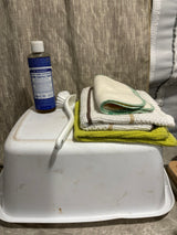 RV rental cleaning essentials: Dr. Bronner's soap, dish brush, & varied cloths on a white basin for compact living.