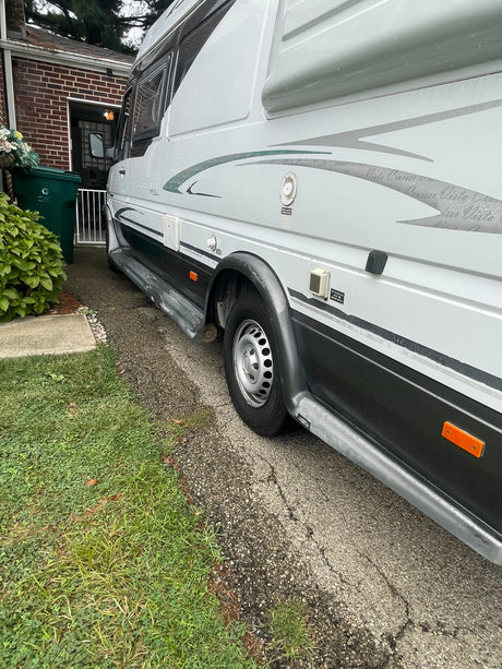 A Vista Cruiser RV rental, a white camper van, is parked on a paved driveway, showcasing its side features and utility access points.