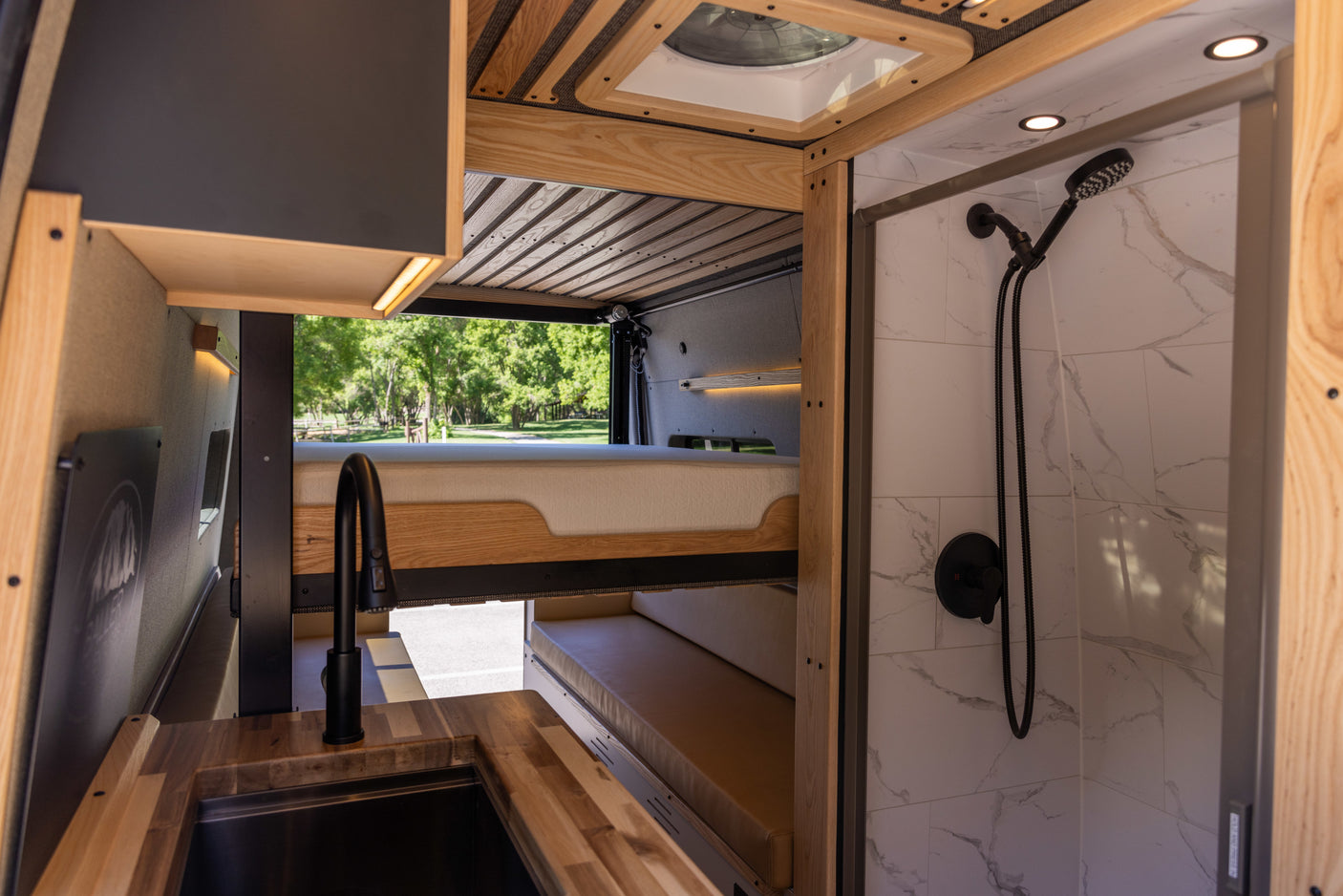 Inside an RV rental: a modern kitchen with wood counters, elevated bed, and tiled shower with black fixtures.