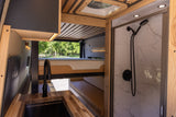 Inside an RV rental: a modern kitchen with wood counters, elevated bed, and tiled shower with black fixtures.