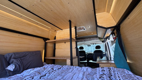 Modern RV rental interior: light wood panels, LED lighting, cozy bed, custom shelves, and front cabin.