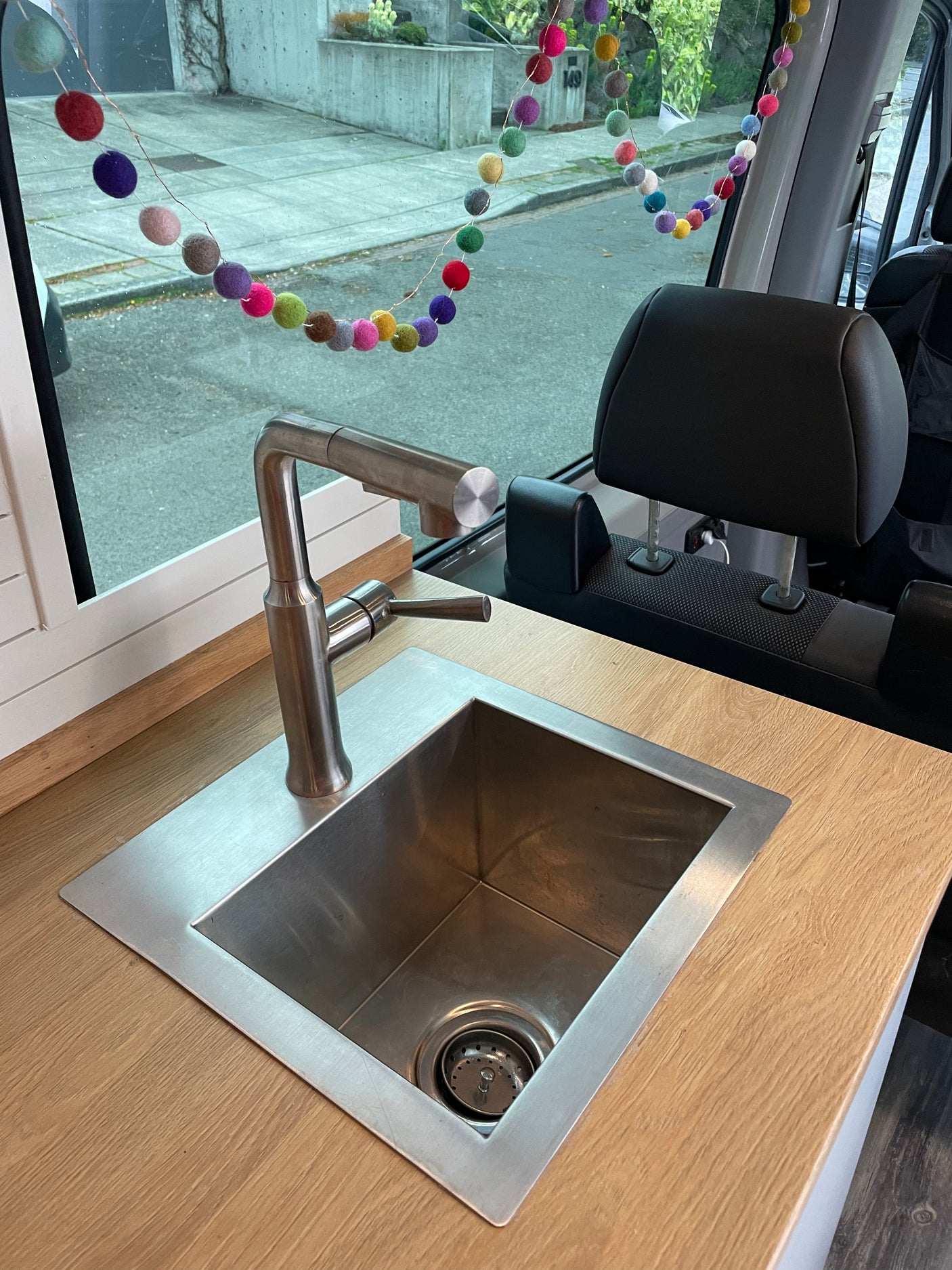 RV rental: Compact kitchen features a modern sink, faucet, and wood counter. Colorful garland hangs in the window.