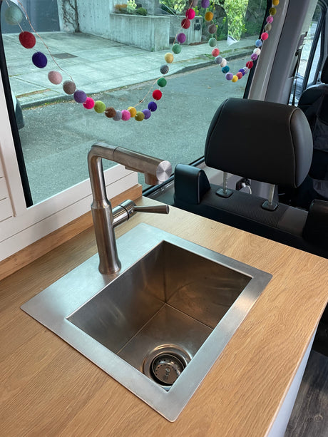 RV rental: Compact kitchen features a modern sink, faucet, and wood counter. Colorful garland hangs in the window.