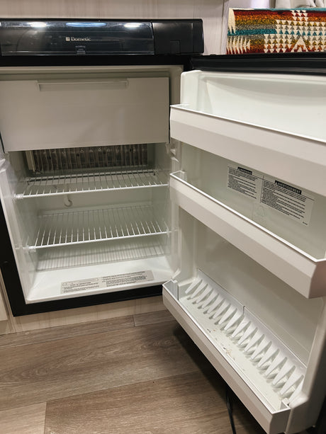 Empty Dometic refrigerator with an open door, revealing its clean, white interior and wire shelves, typical in an rv rental.