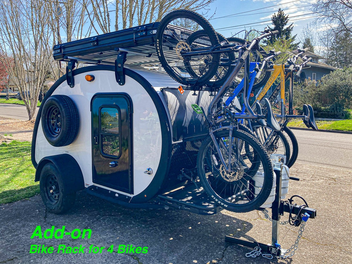 A white teardrop RV rental equipped with a 4-bike rack carrying multiple bicycles and a roof rack system for gear.