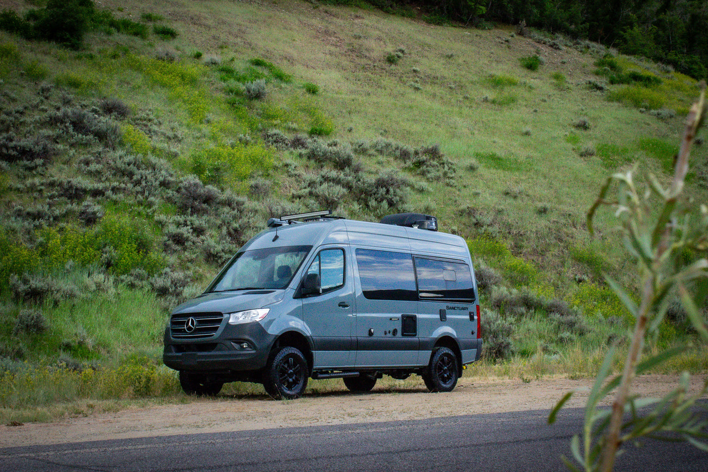 Adventure awaits! A gray Mercedes Sprinter camper van, ideal for rv rental, rests by a scenic, grassy hill.