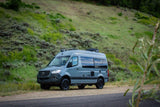 Adventure awaits! A gray Mercedes Sprinter camper van, ideal for rv rental, rests by a scenic, grassy hill.